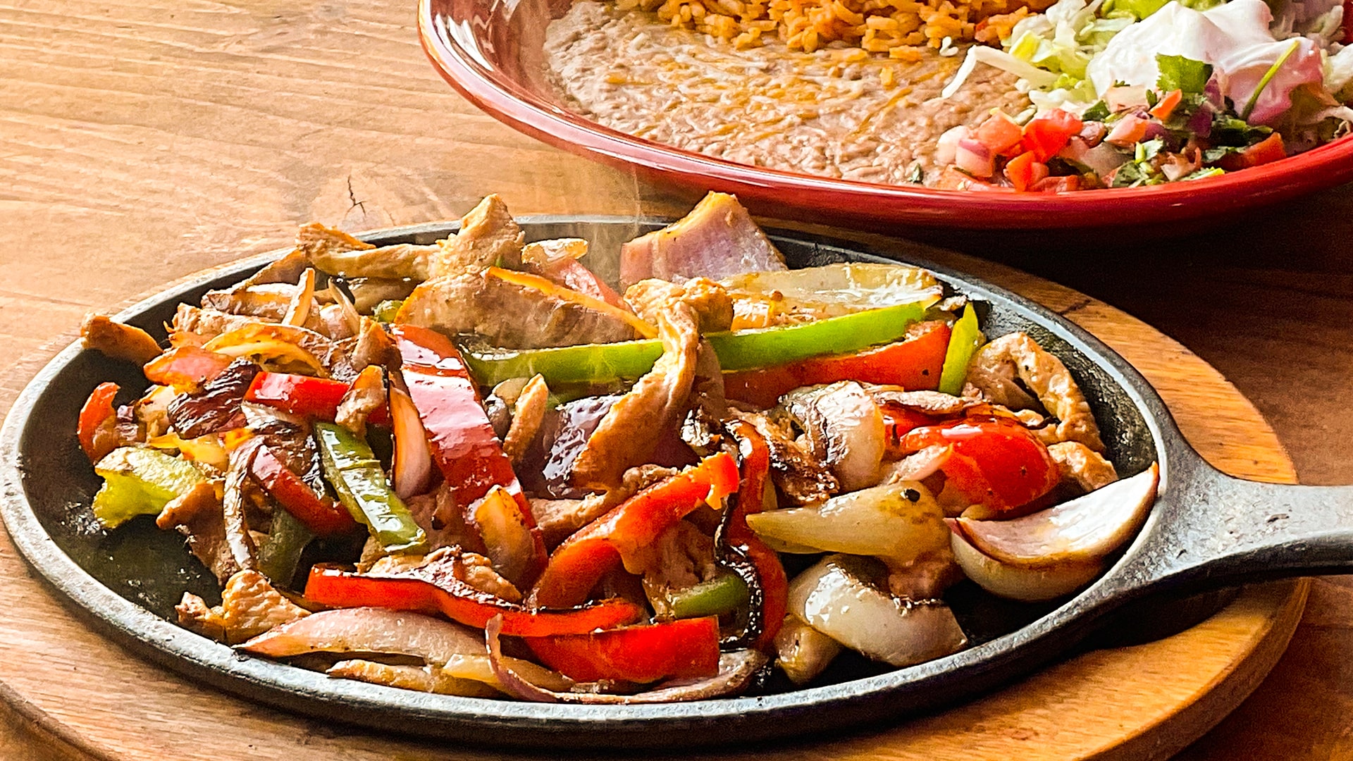 Chicken fajitas with red and green peppers and onions steaming on a black cast iron comal